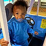 child, toddler, pacifier, blue_hoodie, curly_hair, play_car, steering_wheel, hand, window, door_frame, indoor, sign, martial_arts, kickboxing, jiu_jitsu, floor, toy, cute, portrait, smiling