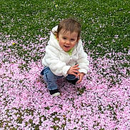 Joy participe au concours pour gagner de l'argent avec cette photo : child, crouching, cute, daylight, face, flower_petals, grass, greenery, happy, jeans, nature, outdoor, person, pink_petals, playing, smiling, socks, spring, toddler, white_jacket