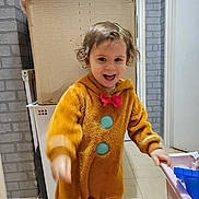 Joy a rejoint le concours — aidez-le/la à gagner de superbes lots ! brown, cardboard_box, child, clothing, costume, curly_hair, cute, gingerbread, happy, home, indoor, motion_blur, person, plastic_bin, playful, red_bow, smiling, tile_floor, toddler, toy_storage