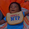 Royal is registered to the contest to win money with this photo: baby, bib, blue_onesie, child, colorful_blanket, expression, face, happy, infant, laying_down, looking_up, moms_mvp, orange_background, person, portrait, smiling, toddler, young_child, clothing, indoor