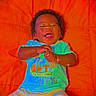 Royal is registered to the contest to win money with this photo: baby, smiling, infant, child, orange_cushion, colorful_clothing, happy, cute, lying_down, portrait, toddler, shorts, hands, face, joyful, bright_colors, indoor, playful, expression, young