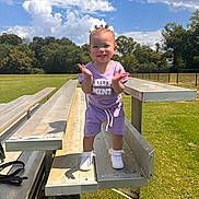 Caríelle is registered to the contest to win money with this photo: toddler, child, smiling, outdoor, bleachers, grass, trees, sky, clouds, purple_clothing, sneakers, sunny, park, happy, person, standing, daylight, expression, cute, fun