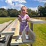 toddler, child, smiling, outdoor, bleachers, grass, trees, sky, clouds, purple_clothing, sneakers, sunny, park, happy, person, standing, daylight, expression, cute, fun