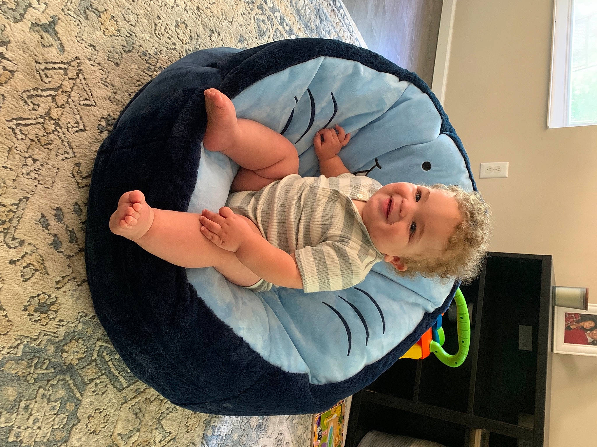 Rio is registered to the contest to win money with this photo: baby, baby_products, baby_toddler_clothing, blurred, child, comfort, elbow, flooring, fun, gesture, human_body, joy, nap, person, picture_frame, play, room, shelf, shoulder, sitting