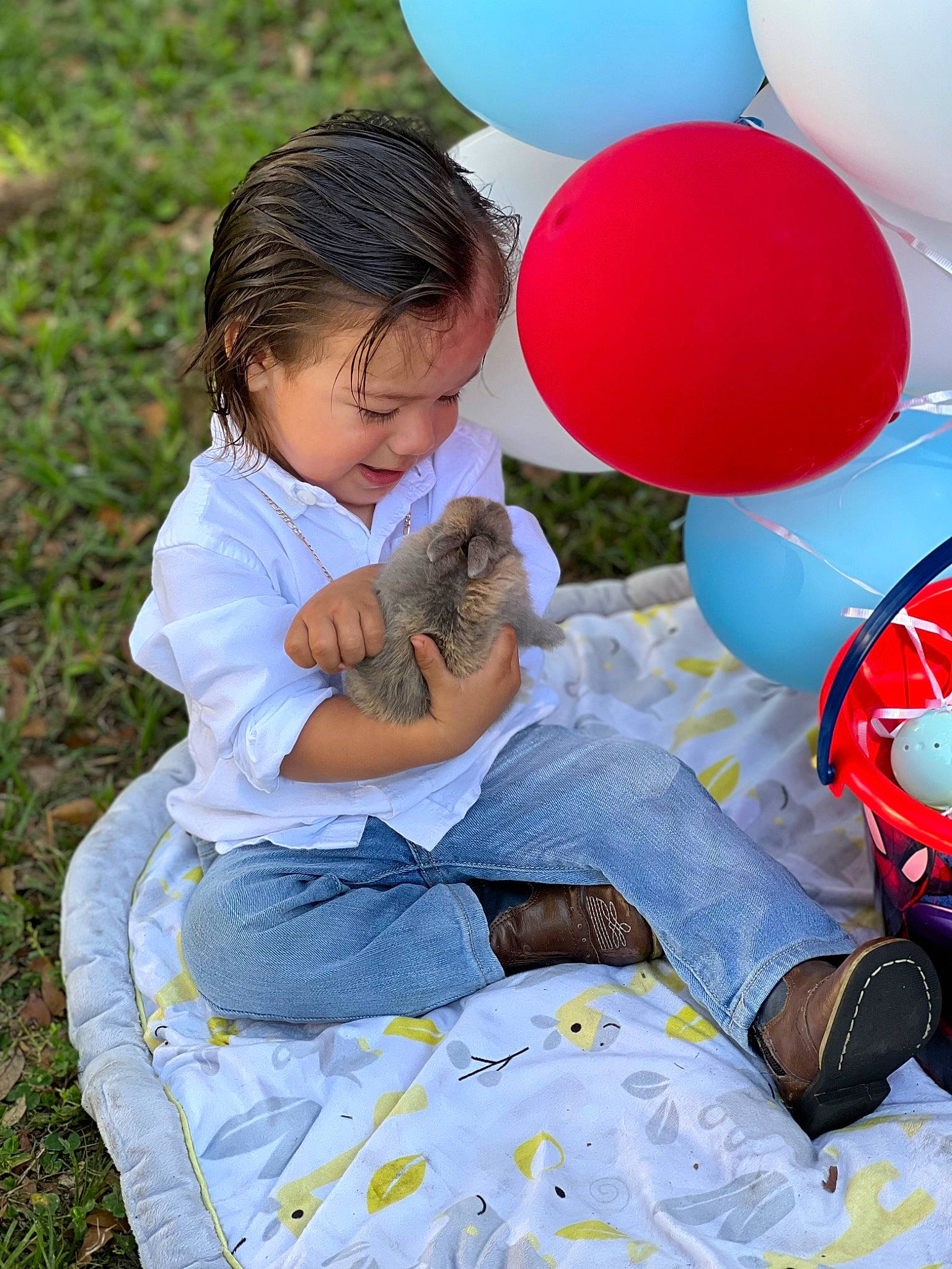 Hezekiah is registered to the contest to win money with this photo: balloon, child, comfort, event, fun, grass, happy, lap, leisure, mammal, party_supply, people_in_nature, person, play, recreation, sharing, sitting, t_shirt, toddler, toy