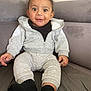 baby, child, smiling, sitting, couch, gray_clothing, black_socks, hoodie, tracksuit, indoors, happy, cute, portrait, person, young_child, cozy, comfortable, curly_hair, wide_eyes, casual