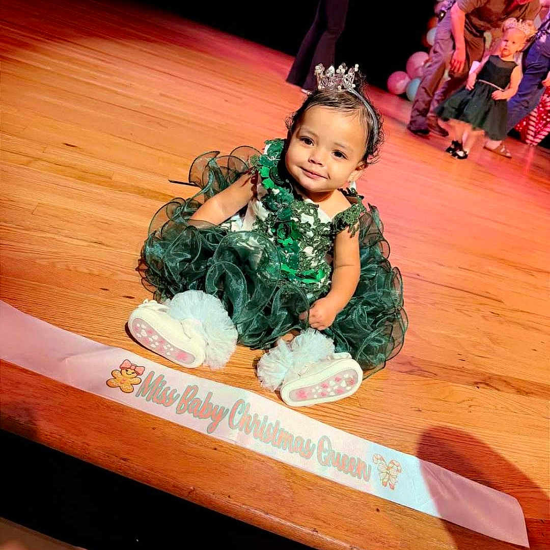 Zoria Rorex is registered to the contest to win money with this photo: baby, balloons, celebration, child, crown, dress, event, festive, girl, green_dress, happy, indoor, people, portrait, sash, smile, stage, tiara, toddler, wooden_floor