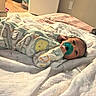 baby, pacifier, bed, blanket, onesie, animal_print, infant, sleepwear, indoors, carpet, doorway, flooring, game_controller, diapers, soft_lighting, child, cute, resting, home, cozy