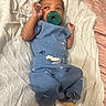baby, infant, pacifier, blue_pajamas, blanket, lying_down, hand_gesture, curly_hair, yellow_socks, soft_texture, indoors, cute, child, sleepwear, resting, infant_clothing, newborn, small_hands, portrait, peaceful