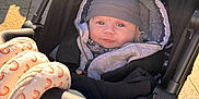 Christopher is registered to the contest to win money with this photo: baby, stroller, beanie, jacket, plush_toy, sunlight, outdoor, child, cute, infant, face, person, warm_clothing, toy, seat, black, gray, patterned_fabric, pacifier, park