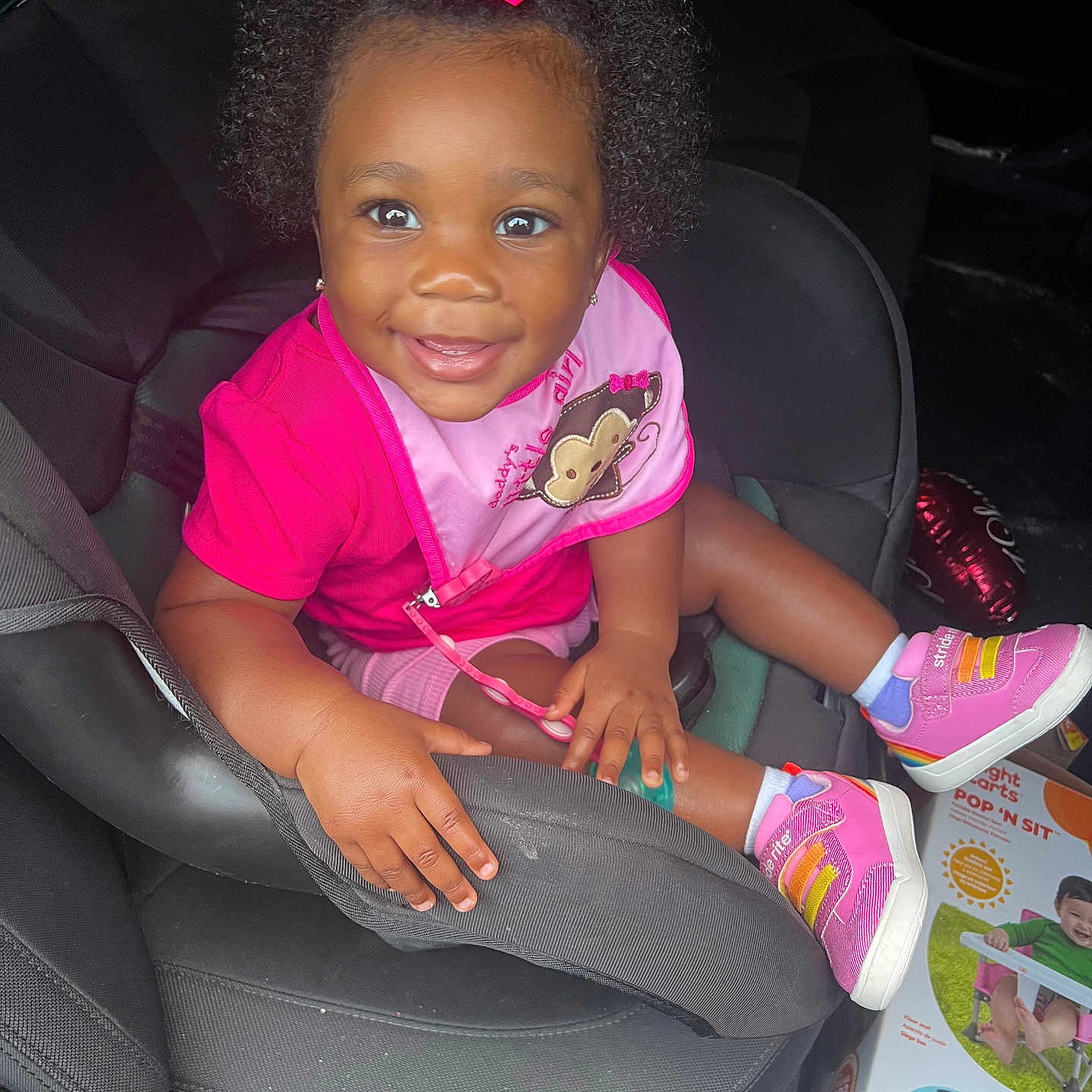 Novi joined the competition — help win amazing prizes! child, toddler, car_seat, pink_bow, pink_shoes, smiling, curly_hair, baby_bib, car_interior, toy_box, balloon, happy, cute, infant, sitting, portrait, clothing, footwear, person, indoors