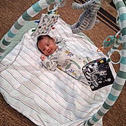 Isaiah is registered to the contest to win money with this photo: baby, infant, blanket, striped_blanket, baby_gym, hanging_toys, elephant_toy, soft_book, floor, carpet, striped_clothing, newborn, cute, lying_down, indoor, child, playtime, relaxed, colorful, toy