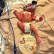 Hunter is registered to the contest to win money with this photo: newborn, baby, hospital, medical_equipment, breathing_mask, sensors, blanket, diaper, sign, text, tubes, monitoring, infant, lying_down, healthcare, cute, child, bed, person, premature