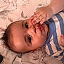 baby, infant, child, face, hand, blue_striped_shirt, lying_down, blanket, pattern, curious, wide_eyes, skin, mouth, nose, hair, cute, indoors, playful, expression, young