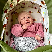 Ophelia is registered to the contest to win money with this photo: baby, smiling, infant, pink_sweater, knitted_hat, blanket, stroller, hedgehog_pattern, butterfly_pattern, cozy, cute, child, portrait, happy, indoor, fabric, clothing, face, person, cute_baby