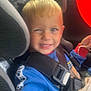 Lucas is registered to the contest to win money with this photo: blond_hair, blue_shirt, car_interior, car_seat, casual_clothing, child, cute, fabric, face, happy, kid, portrait, red_balloon, seat_belt, seatbelt, sitting, smiling, toddler, vehicle, window