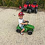 Lucas is registered to the contest to win money with this photo: boy, cap, child, concrete, daytime, fence, footwear, grass, green_toy, happy, outdoor, plants, play, red_toy, shorts, smile, spiderman, toy_tractor, tshirt, vehicle