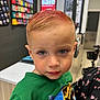 blue_eyes, boy, casual, child, closeup, clothing, counter, curious, dinosaur, display, face, green_shirt, hair, holding, indoor, person, portrait, short_hair, sign, store
