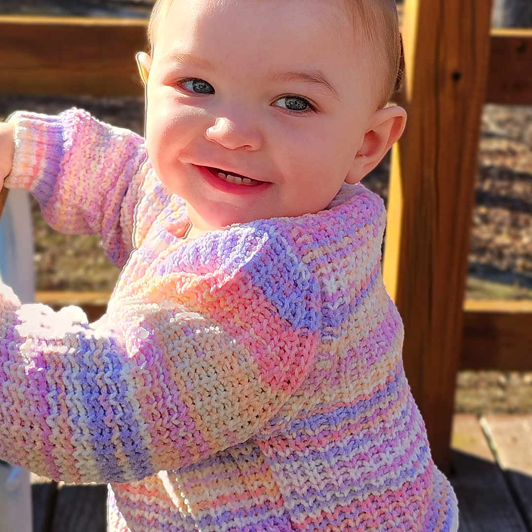 Hazel joined the competition — help win amazing prizes! toddler, child, smiling, outdoor, knitted_sweater, colorful_clothing, jeans, railing, wooden_deck, sunlight, happy, face, portrait, cute, baby, standing, nature, daylight, person, casual