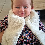 Djulia participe au concours pour gagner de l'argent avec cette photo : baby, child, smile, indoor, floral_clothing, white_vest, fur_texture, happy, cute, portrait, person, tiled_floor, table, hair, face, sitting, young_child, apparel, fashion, cozy
