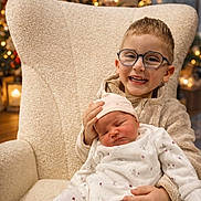 Rachel a rejoint le concours — aidez-le/la à gagner de superbes lots ! child, baby, glasses, smiling, sleeping, chair, holiday_lights, christmas_tree, cozy_clothing, indoor, family, cute, infant, toddler, warm_lighting, festive, decorations, happy, portrait, seated