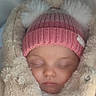 baby, sleeping, pink_hat, pom_poms, beige_coat, blanket, soft_texture, cute, infant, warm_clothing, face, closed_eyes, bundle_up, cozy, winter, child, portrait, indoor, headwear, peaceful