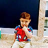 child, toddler, boy, portrait, sitting, stone_ledge, indoor, spiderman_shirt, superhero, colorful_clothing, shorts, sneakers, brown_hair, side_glance, finger_in_mouth, serious_expression, dark_background, marble, watermark, photography