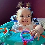 Aurora is registered to the contest to win money with this photo: baby, child, smiling, pigtails, toys, baby_seat, colorful, happy, indoor, cute, person, playful, clothing, face, hand, infant, furniture, bright, young, cheerful