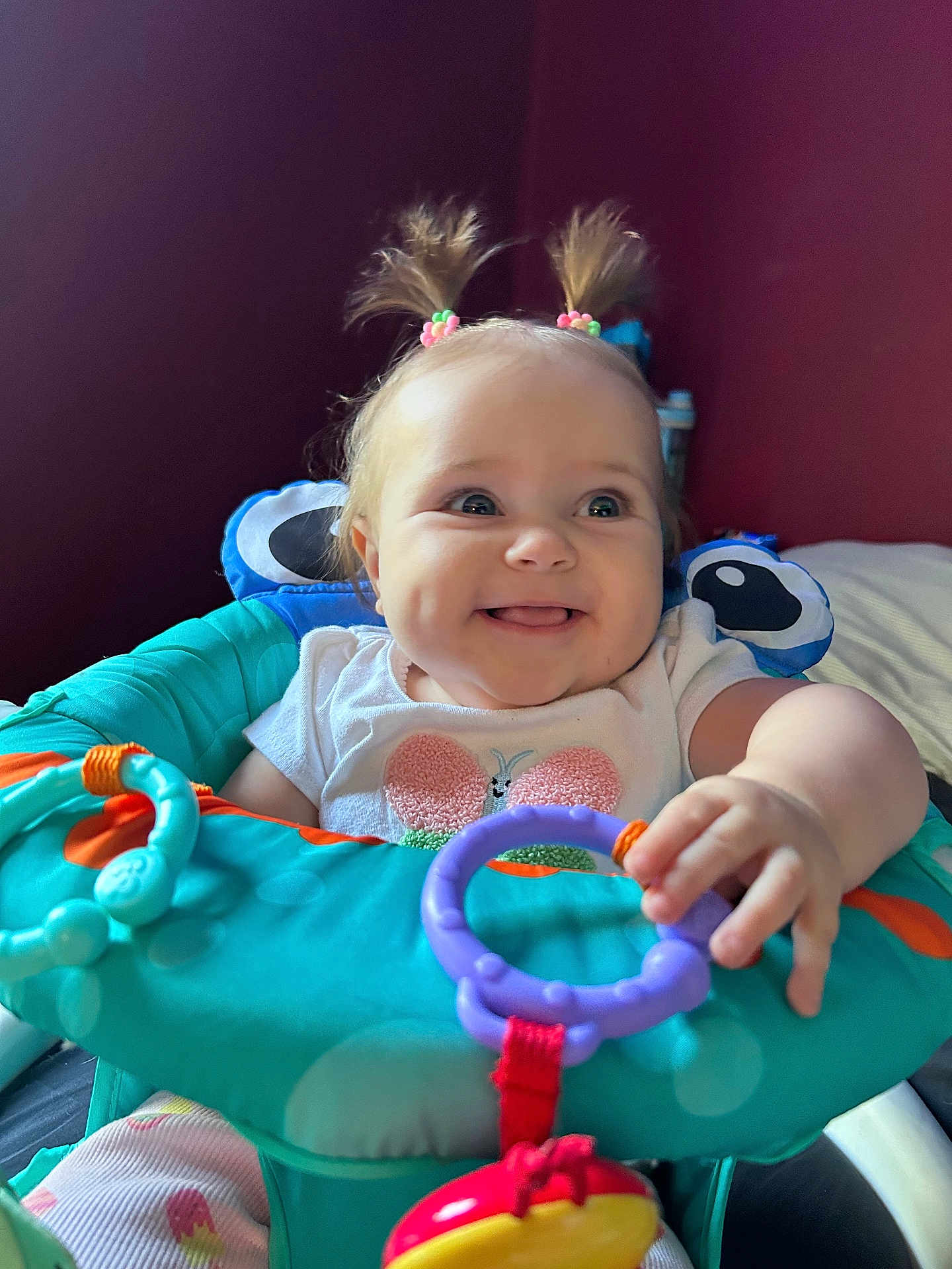 Aurora is registered to the contest to win money with this photo: baby, child, smiling, pigtails, toys, baby_seat, colorful, happy, indoor, cute, person, playful, clothing, face, hand, infant, furniture, bright, young, cheerful