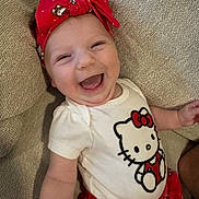 Malia joined the competition — help win amazing prizes! baby, child, smiling, laughing, headband, red_headband, hello_kitty, white_shirt, red_shorts, couch, beige_couch, happy, cute, infant, person, indoor, portrait, clothing, fabric, head