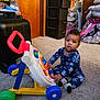 Raven is registered to the contest to win money with this photo: baby, child, toy, walker, carpet, indoor, onesie, patterned_clothing, floor, storage_drawer, luggage, baby_gear, mirror, colorful, play, curious, sitting, footwear, room, wooden_door