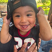 Jayava is registered to the contest to win money with this photo: baby, black_cap, cap, child, clothing, cute, eyes, face, hands, happy, holding, joy, number_23, outdoor, person, portrait, shirt, skin, smiling, toddler
