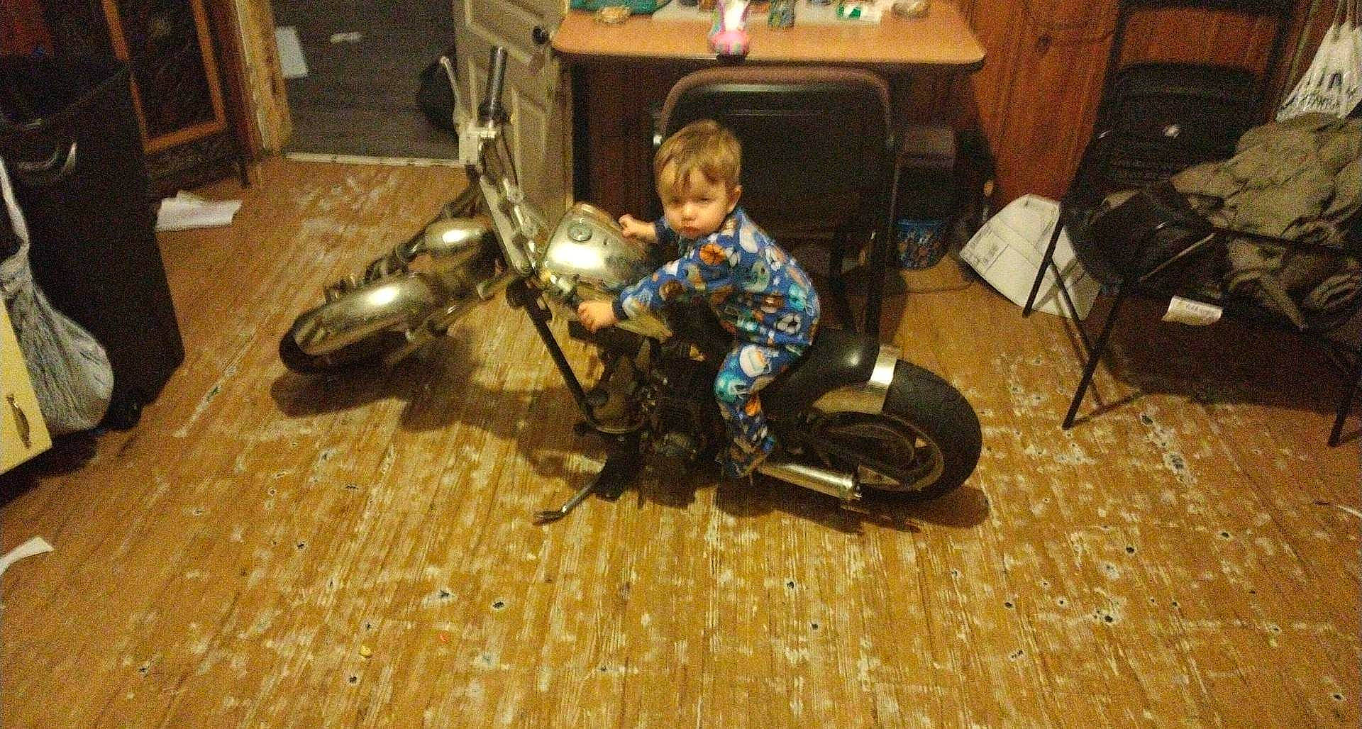 Deegan is registered to the contest to win money with this photo: automotive_design, automotive_lighting, automotive_tire, cabinetry, chair, comfort, drawer, fender, floor, flooring, hardwood, motor_vehicle, motorcycle, person, tire, toddler, toy, tread, vehicle, wheel