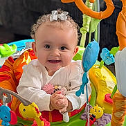 Mariska is registered to the contest to win money with this photo: activity_center, baby, bright_eyes, child, closeup, colorful, curly_hair, cute, hands_clasped, happy, indoor, infant, plastic_toys, play, playful, portrait, seat, smiling, toy, white_bow
