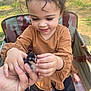 child, toddler, baby, person, face, smile, curly_hair, eyelashes, chick, bird, animal, hand, holding, outdoor, nature, chair, camouflage, brown_shirt, black_pants, happy