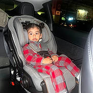 Soham is registered to the contest to win money with this photo: child, toddler, car_seat, car_interior, seatbelt, red_clothing, checkered_pattern, hair_buns, indoor, parking_garage, window, seat, young_child, casual_clothing, socks, curious_expression, vehicle, safety, infant, portrait