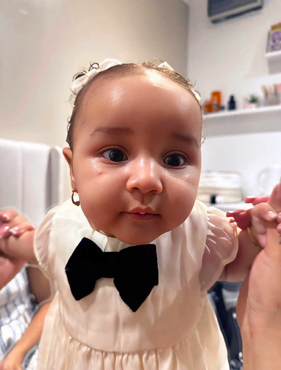 Anela is registered to the contest to win money with this photo: baby, child, closeup, portrait, indoor, dress, bow_tie, adorable, cute, face, hands, curious, small_earring, infant, person, skin, head, expression, clothing, young