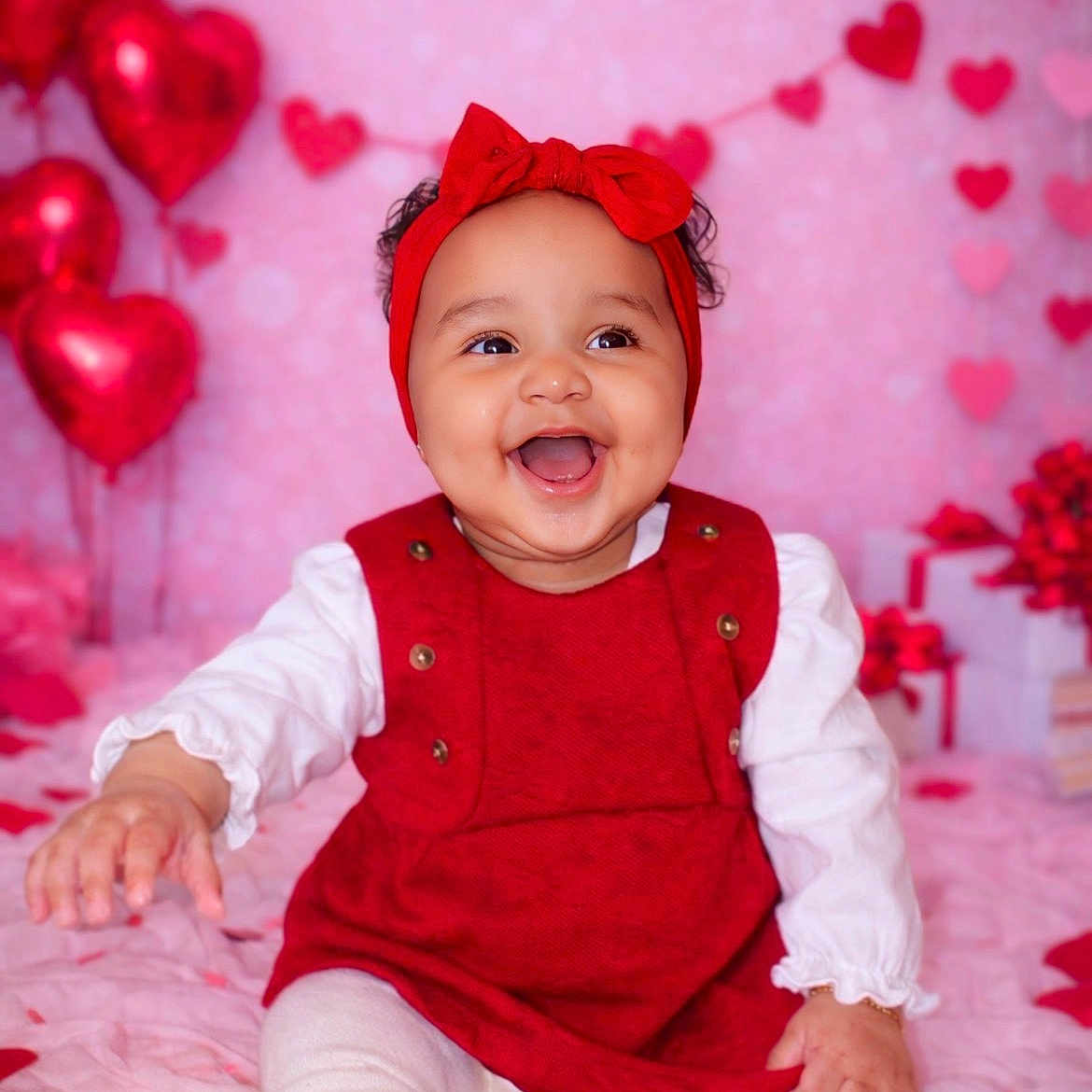Anela joined the competition — help win amazing prizes! baby, balloons, blanket, chubby_cheeks, cute, gift_boxes, happy, heart_garland, hearts, infant, pink_background, portrait, red_dress, red_headband, sitting, smiling, studio_photo, valentine_theme, white_tights, wrapped_gifts