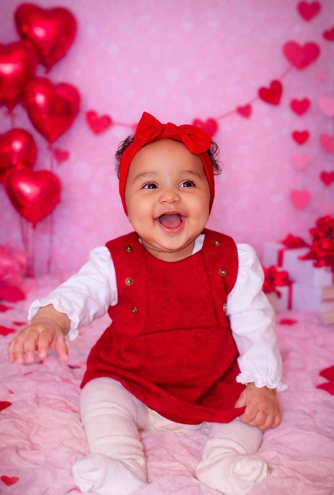 Anela joined the competition — help win amazing prizes! baby, infant, smiling, red_headband, red_dress, hearts, balloons, valentine_theme, pink_background, sitting, portrait, happy, cute, gift_boxes, wrapped_gifts, heart_garland, blanket, white_tights, studio_photo, chubby_cheeks