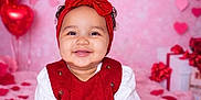 Anela joined the competition — help win amazing prizes! baby, toddler, smile, red_dress, headband, bow, valentines, heart_balloons, pink_background, garland, gift_boxes, sitting, portrait, studio, happy, rosy_cheeks, blanket, hands, cute, festive