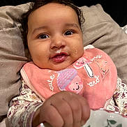 Anela is registered to the contest to win money with this photo: baby, infant, smiling, bib, cute, face, hand, closeup, child, portrait, clothing, cushion, soft, happy, indoor, person, expression, holding, food, messy