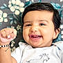 Aaira joined the competition — help win amazing prizes! baby, smiling, infant, face, hand, white_onesie, goat_drawing, black_hair, happy, cute, portrait, closeup, indoor, child, fist, flower_pattern, background, skin, young, cheerful