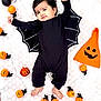 baby, bare_feet, bat_costume, black_clothing, celebration, child, costume, cute, cute_face, decorations, festive, halloween, holiday, indoors, infant, lying_down, orange_pumpkin_lights, pumpkin_hat, smiling_pumpkin, soft_blanket