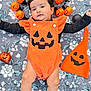 Aaira joined the competition — help win amazing prizes! baby, black_sleeves, blanket, child, costume, cute, decorations, festive, floral_pattern, halloween, hat, holiday, indoors, infant, laying_down, orange_outfit, person, pumpkin_face, pumpkin_lights, smiling