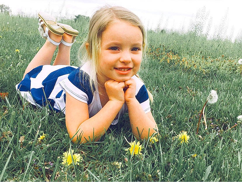 Ryley is registered to the contest to win money with this photo: daytime, facial_expression, finger, flower, fun, gesture, grass, grass_family, grassland, happy, joy, lawn, meadow, natural_environment, people_in_nature, person, plant, sky, smile, sunlight