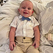 Archie is registered to the contest to win money with this photo: baby, child, smiling, bow_tie, shirt, shorts, bed, blanket, bottle, indoor, cute, infant, happy, person, clothing, sitting, face, skin, comfort, young