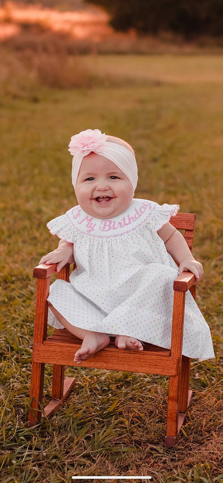 Palmer is registered to the contest to win money with this photo: baby, baby_toddler_clothing, chair, dress, eye, face, fun, grass, happy, headwear, human_body, joy, pattern, people_in_nature, person, photograph, pink, plant, skin, sleeve