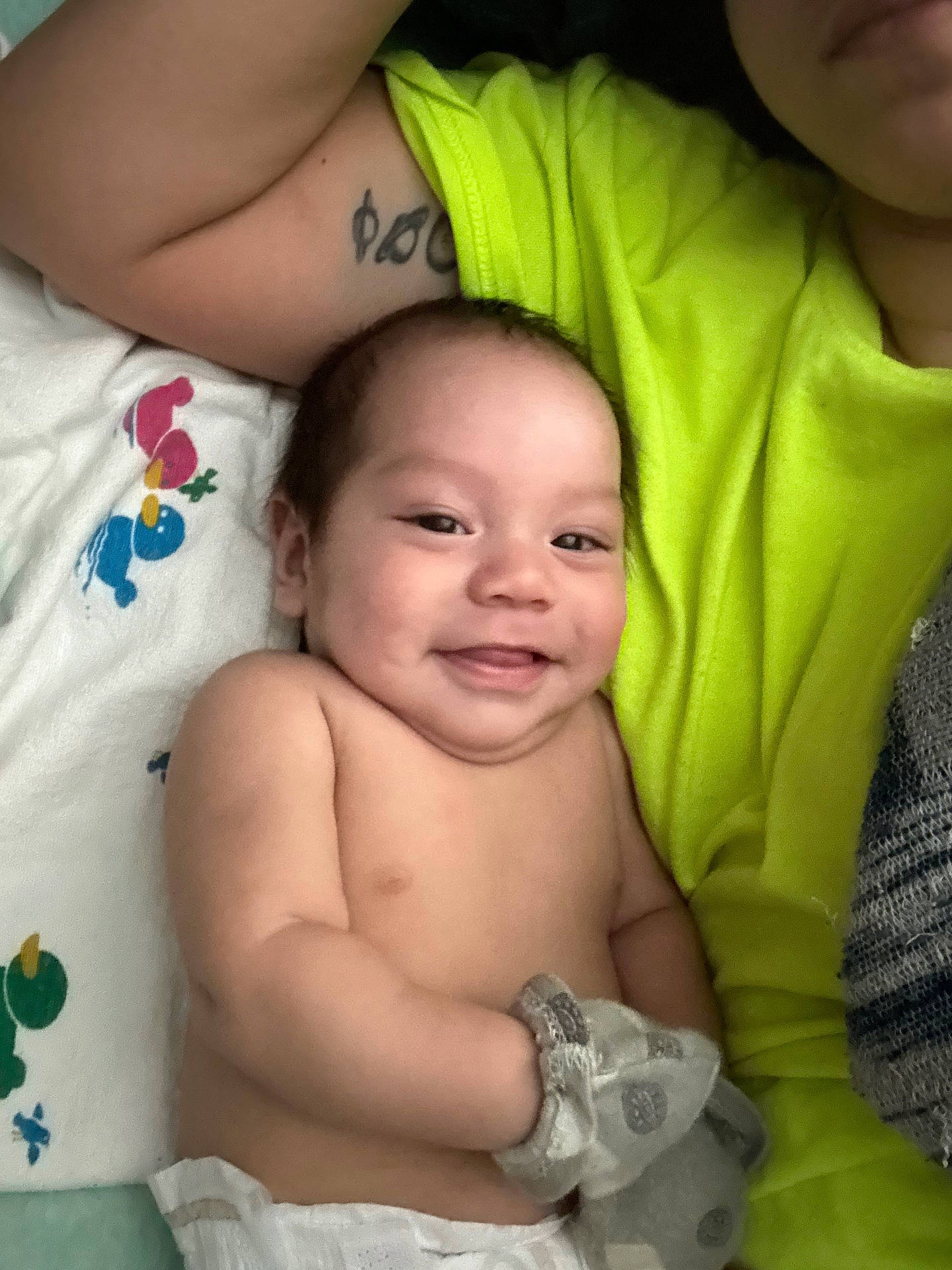 Francisco is registered to the contest to win money with this photo: baby, blanket, child, closeup, cute, diaper, family, happy, human, indoor, infant, lying_down, mittens, person, portrait, relaxed, skin, smiling, tattoo, yellow_shirt