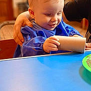 Brooks joined the competition — help win amazing prizes! adult, background_blur, blue_smock, bright, cardboard_tube, child, curious, face, furniture, hand, happy, indoor, light, person, play, smiling, support, table, toddler, young_child