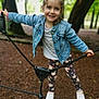 child, girl, smiling, denim_jacket, leggings, white_shoes, rope, playground, outdoor, forest, tree, nature, happy, casual_clothing, young, fun, active, daylight, portrait, cute